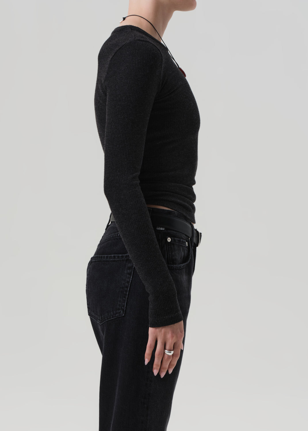 Person wearing a charcoal long-sleeve top and black pants on a light gray background