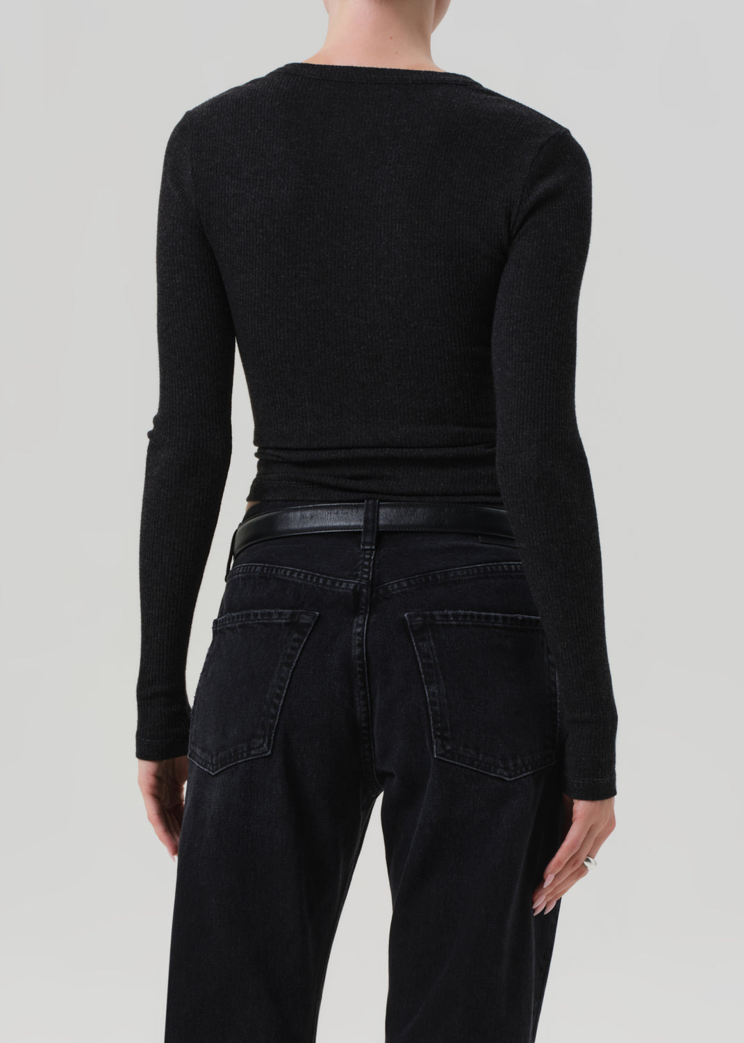 Person wearing a charcoal long-sleeve top and black pants on a light gray background