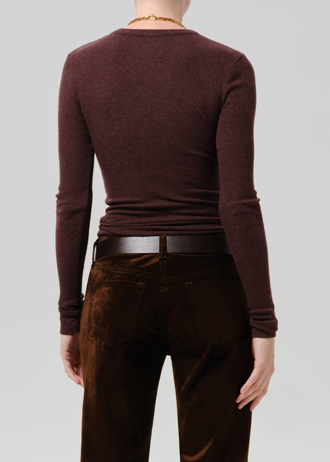 Rear view of a person wearing a fitted long-sleeve crew-neck top in deep burgundy, paired with dark brown pants and a black belt, against a grey background.