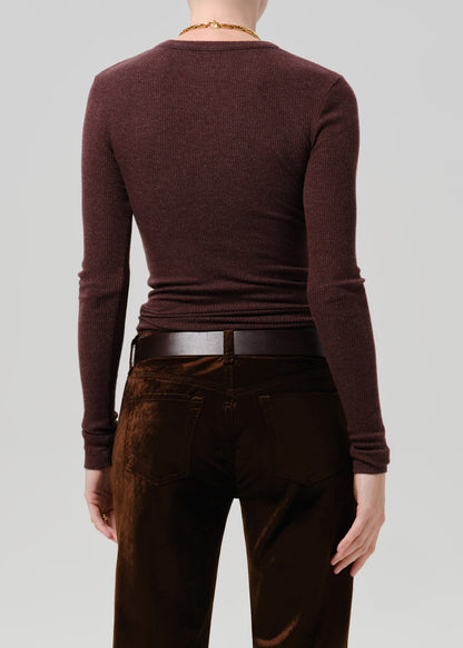 Rear view of a person wearing a fitted long-sleeve crew-neck top in deep burgundy, paired with dark brown pants and a black belt, against a grey background.