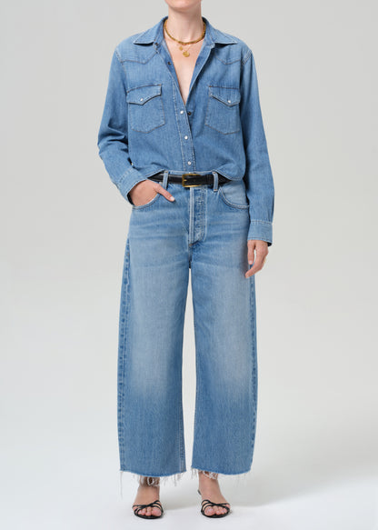 Person wearing a blue denim shirt and jeans on a gray background