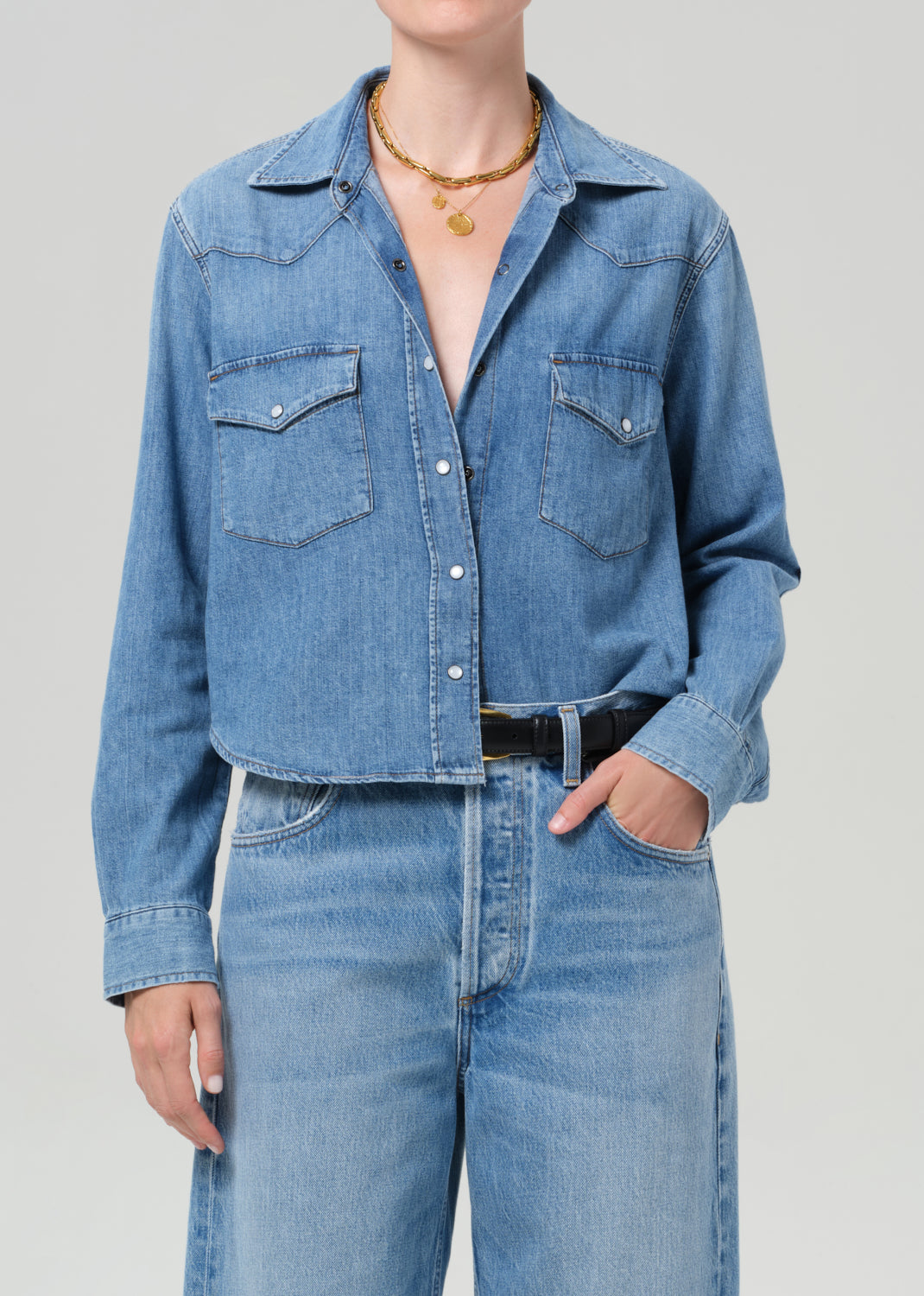 Person wearing a blue denim shirt and jeans on a gray background