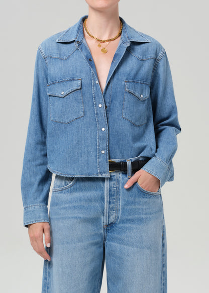 Person wearing a blue denim shirt and jeans on a gray background