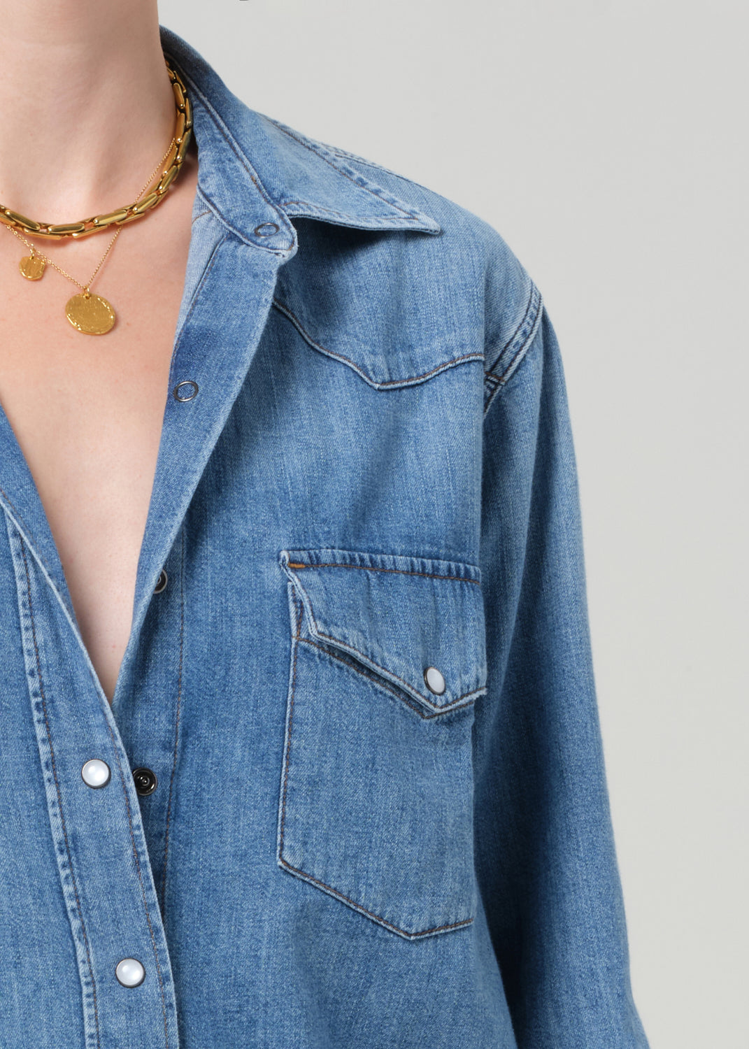 Person wearing a blue denim shirt and jeans on a gray background