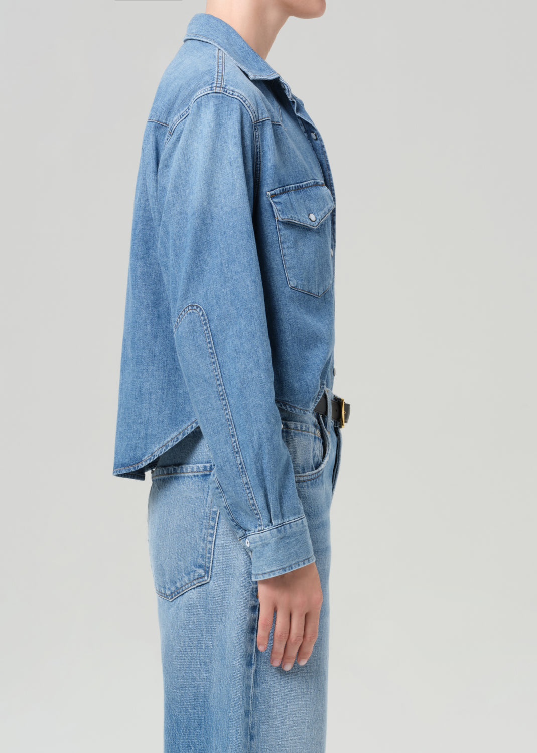 Person wearing a blue denim shirt and jeans on a gray background