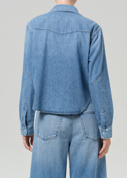 Person wearing a blue denim shirt and jeans on a gray background