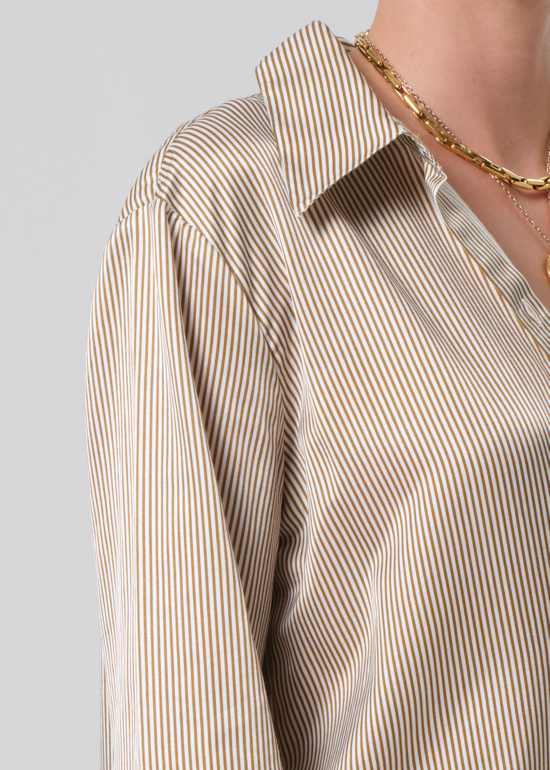 Close-up of a person wearing a beige and white striped shirt with a gold chain on a gray background