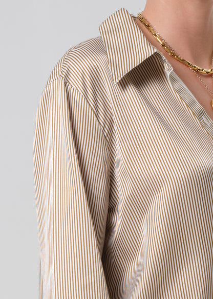 Close-up of a person wearing a beige and white striped shirt with a gold chain on a gray background
