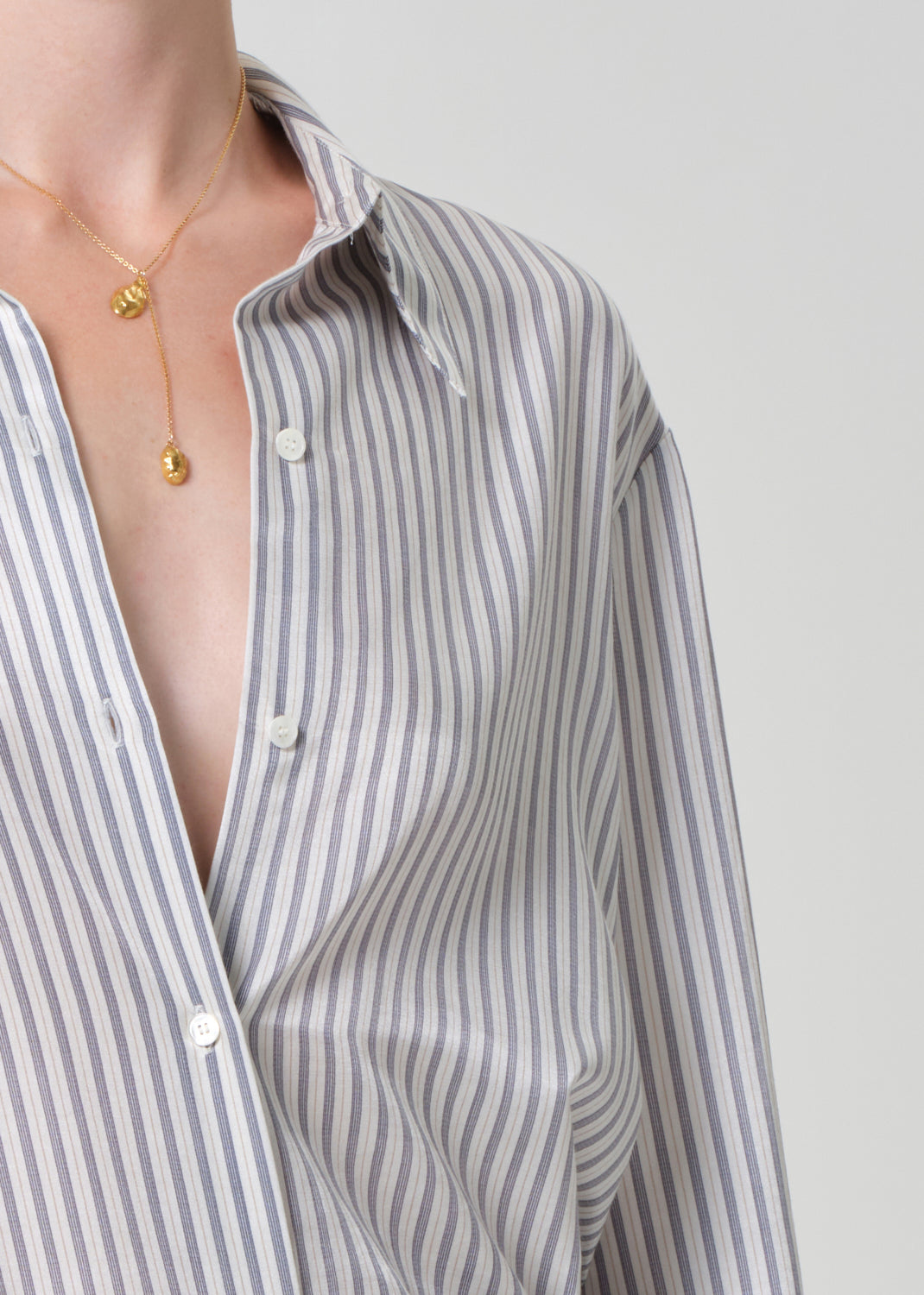Person wearing a striped shirt with a necklace on a plain background