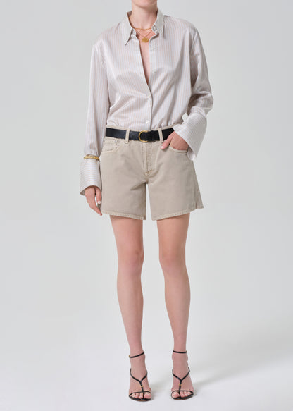 Person wearing a light striped shirt and beige shorts on a plain background