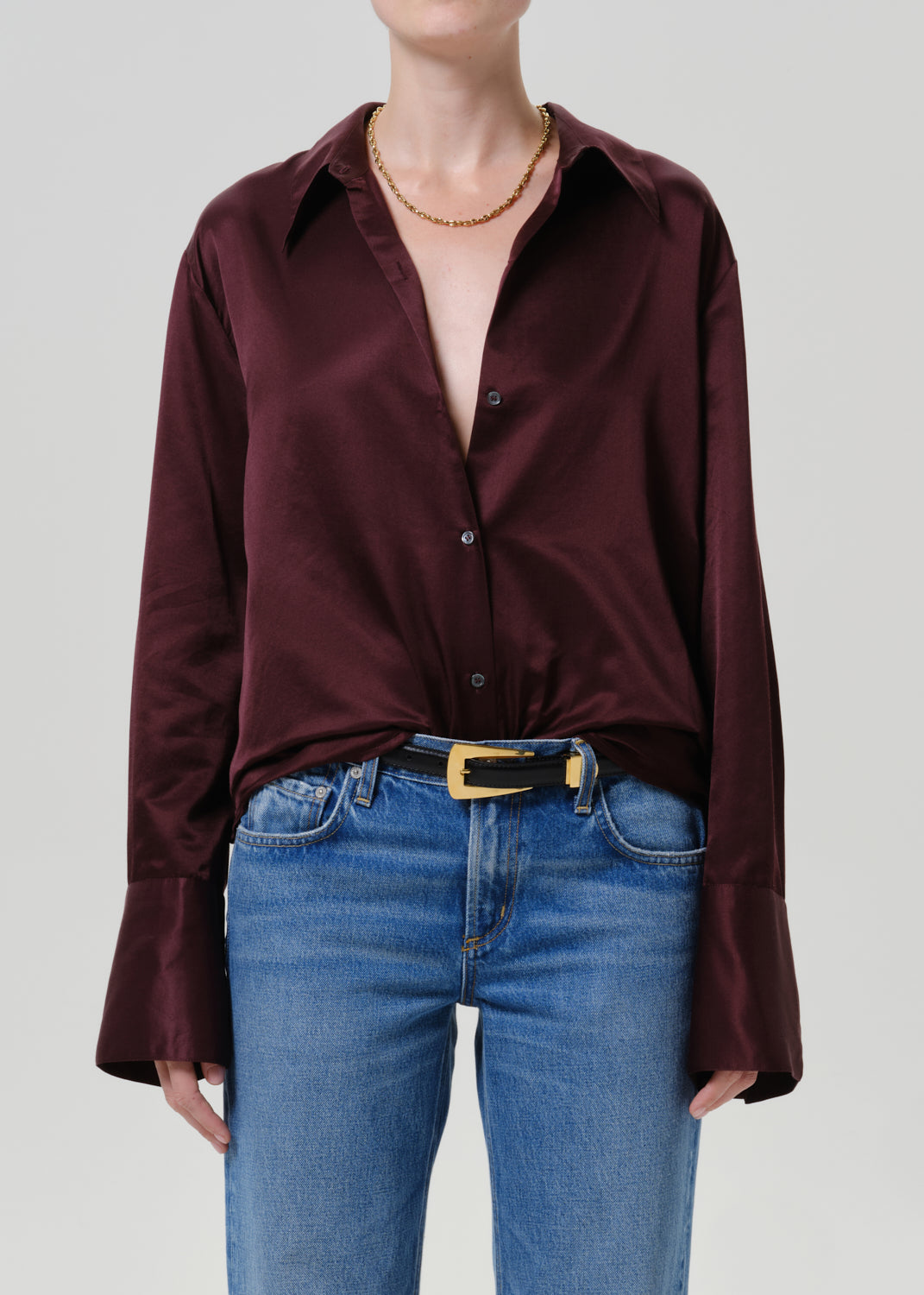 Woman wearing a burgundy satin button-up shirt with medium blue straight leg jeans on a grey background.