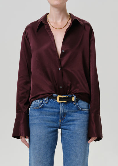 Woman wearing a burgundy satin button-up shirt with medium blue straight leg jeans on a grey background.