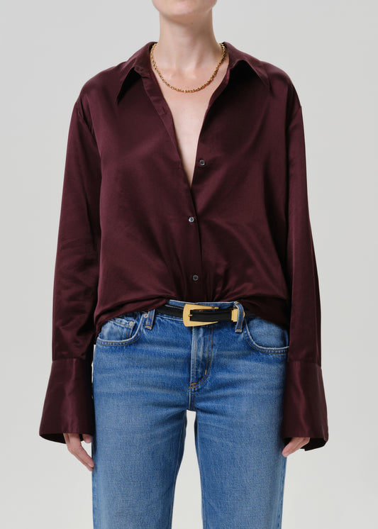 Woman wearing a burgundy satin button-up shirt with medium blue straight leg jeans on a grey background.