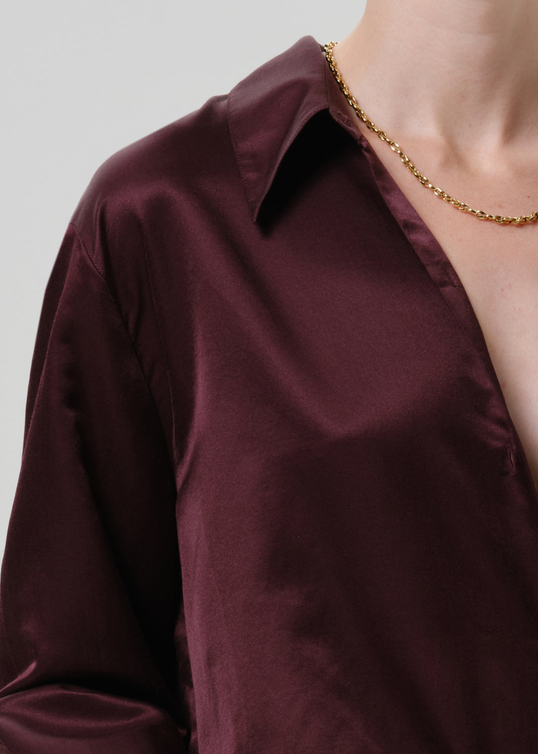 Close-up of a burgundy satin button-up shirt on a grey background.