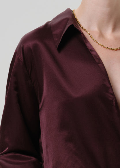 Close-up of a burgundy satin button-up shirt on a grey background.