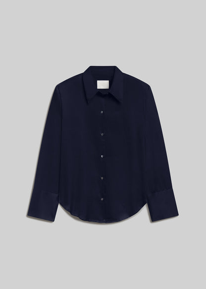 Midnight navy long-sleeve button-down shirt with a pointed collar, front button closure, wide cuffs, and curved hem, front flat lay view on a grey background.