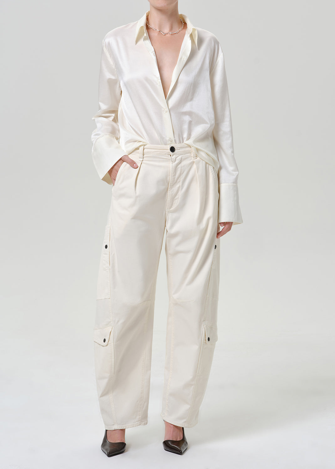 Woman wearing a white satin button-up shirt with white wide leg pants on a grey background.