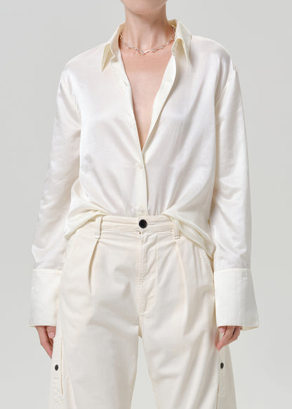 Woman wearing a white satin button-up shirt with white wide leg pants on a grey background.