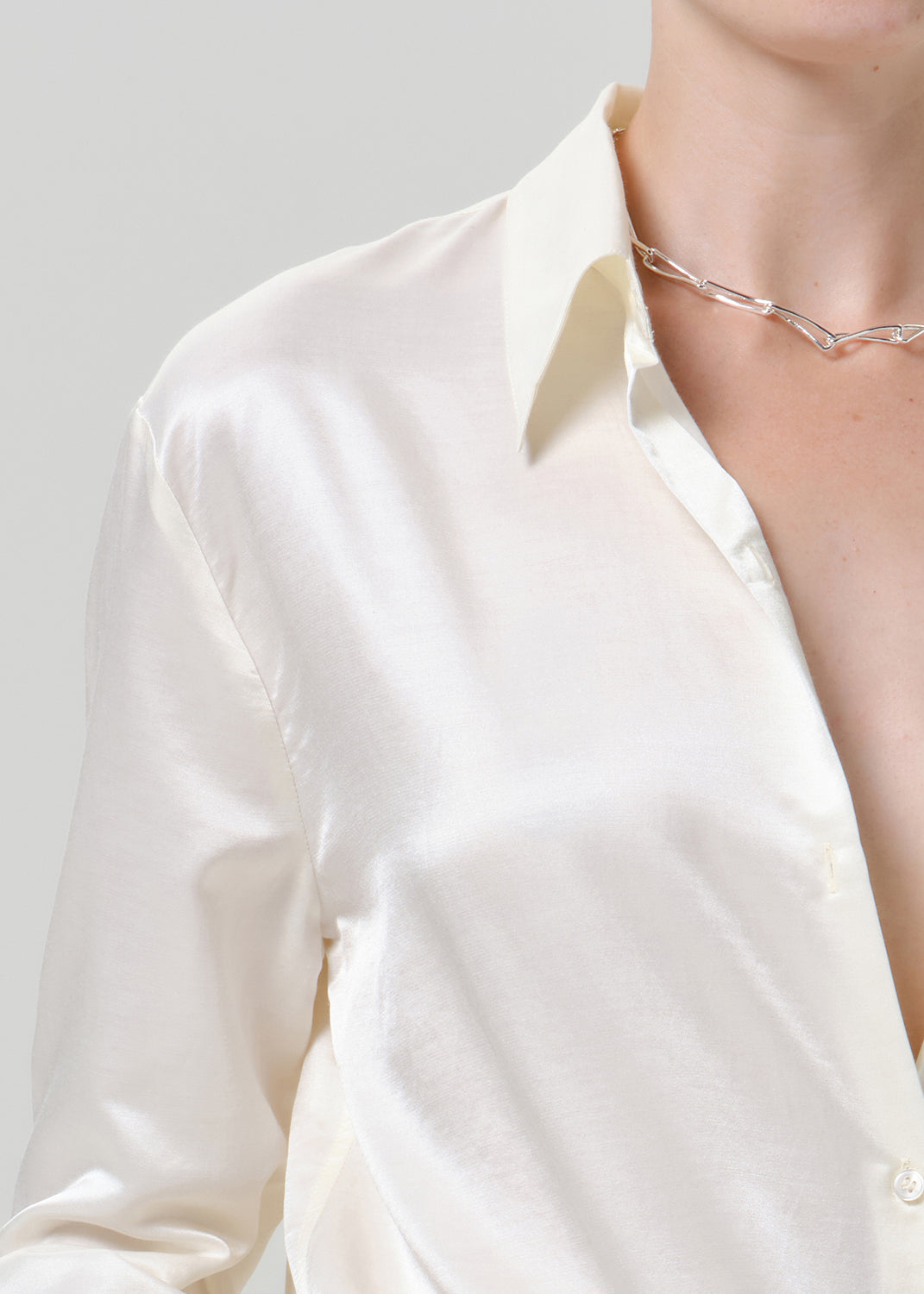 Close-up of a white satin button-up shirt on a grey background.