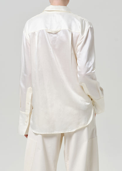 Woman wearing a white satin button-up shirt with white wide leg pants viewed from the back on a grey background.