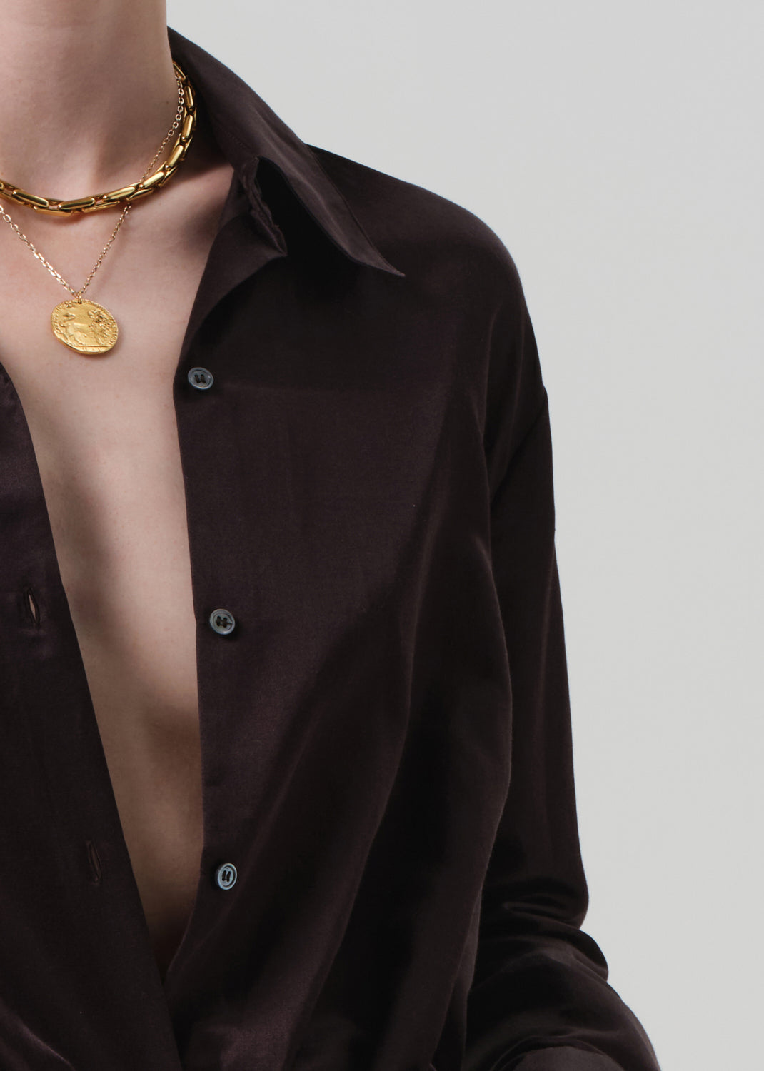 Person wearing a brown shirt and white pants with a plain background