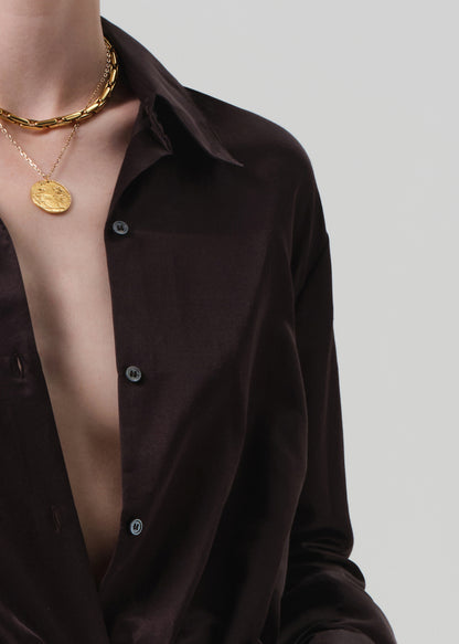 Person wearing a brown shirt and white pants with a plain background