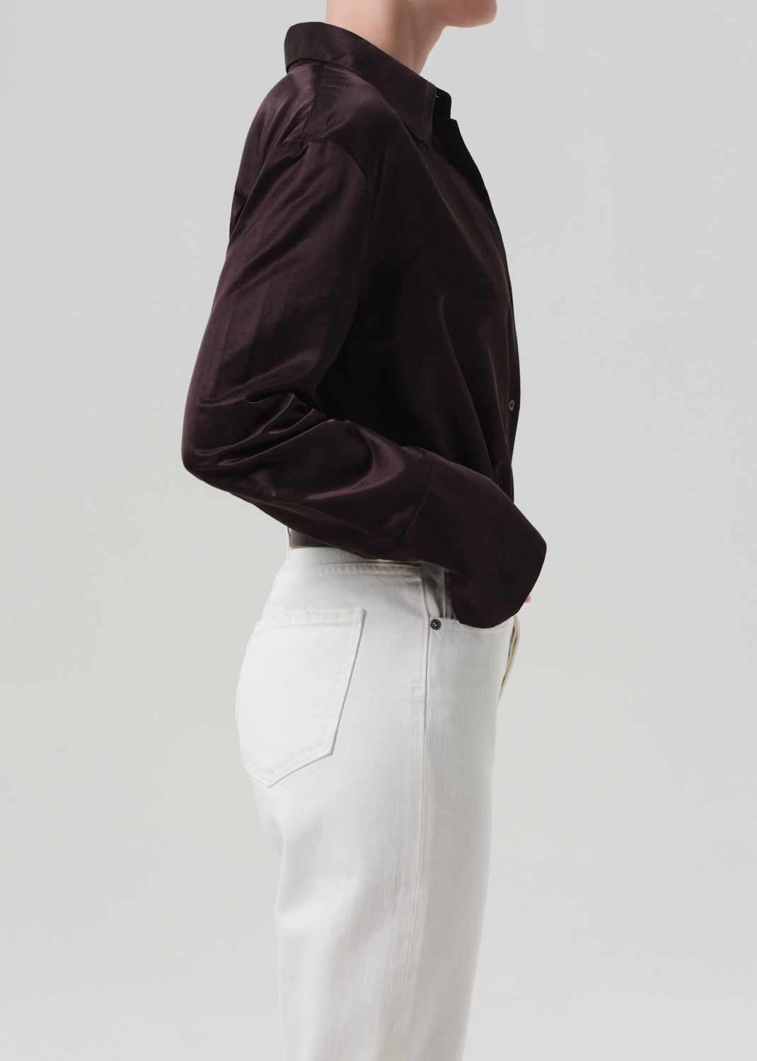 Person wearing a brown shirt and white pants with a plain background