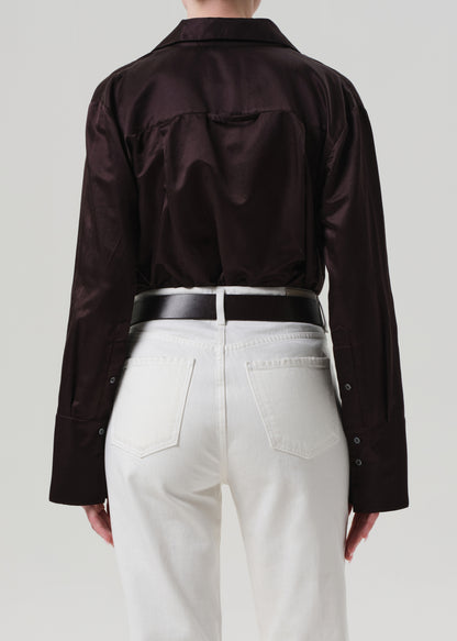 Person wearing a brown shirt and white pants with a plain background