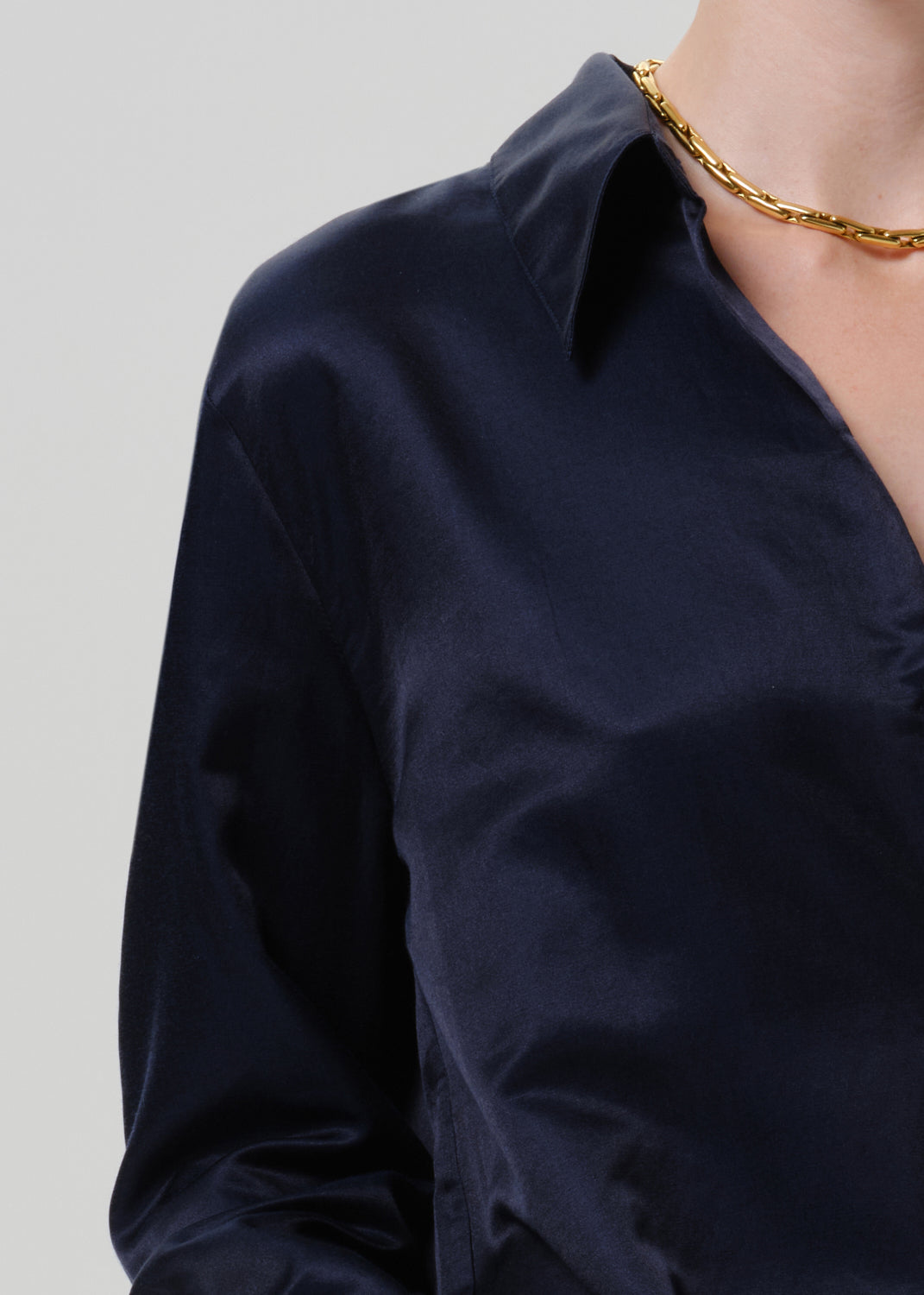 Close-up of a dark navy satin button-up shirt on a grey background.