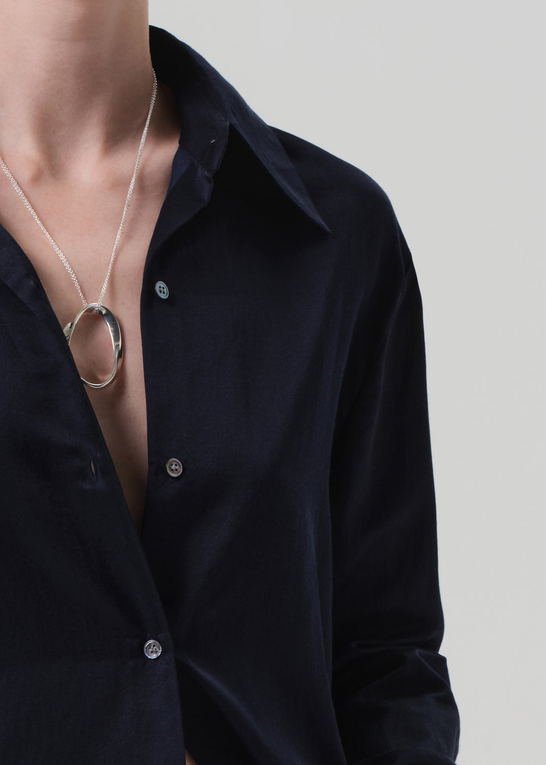 Person wearing a navy shirt with a necklace featuring two interlocking rings on a neutral background