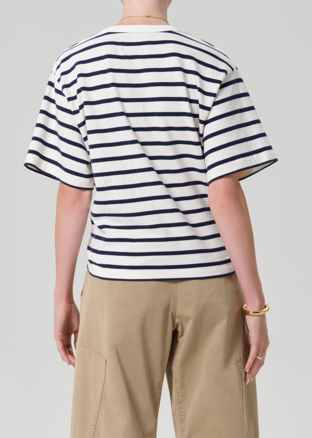 Person wearing a striped shirt and beige pants on a plain background