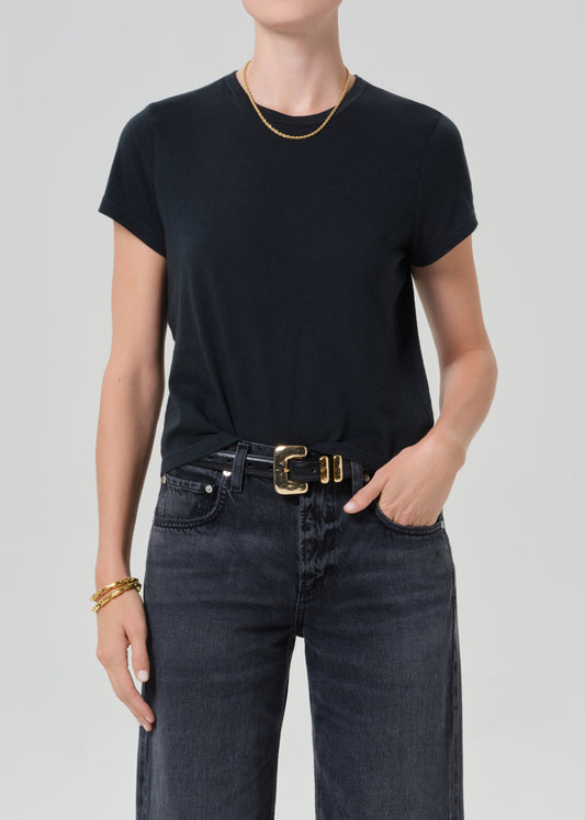 Person wearing a black t-shirt and washed black jeans with a gold belt on a light gray background