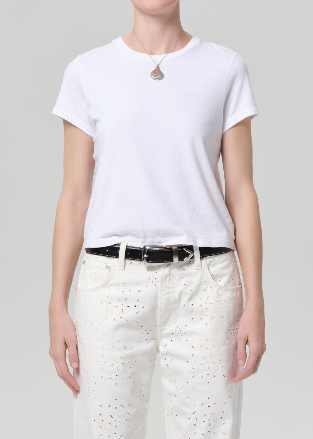 Person wearing a white t-shirt and white pants with a belt on a plain background