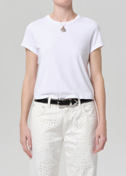 Person wearing a white t-shirt and white pants with a belt on a plain background
