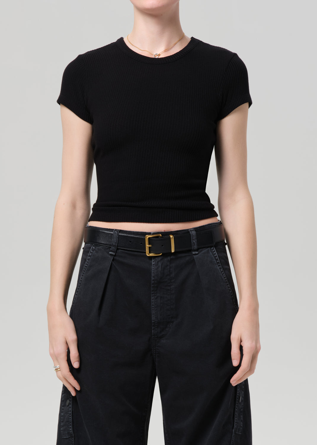 Person wearing a black ribbed tee and black cargo pants on a light gray background