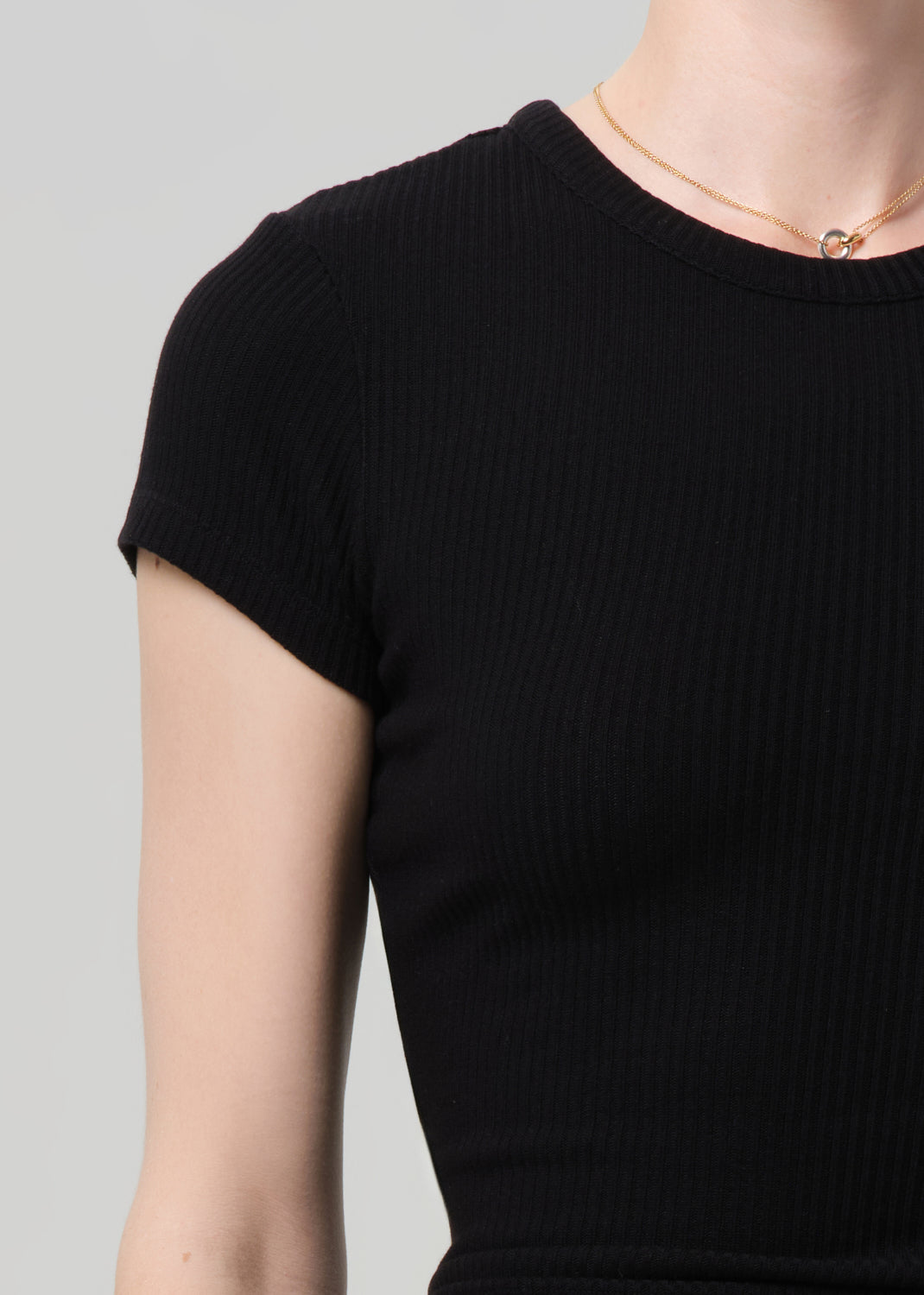 Person wearing a black ribbed tee and black cargo pants on a light gray background