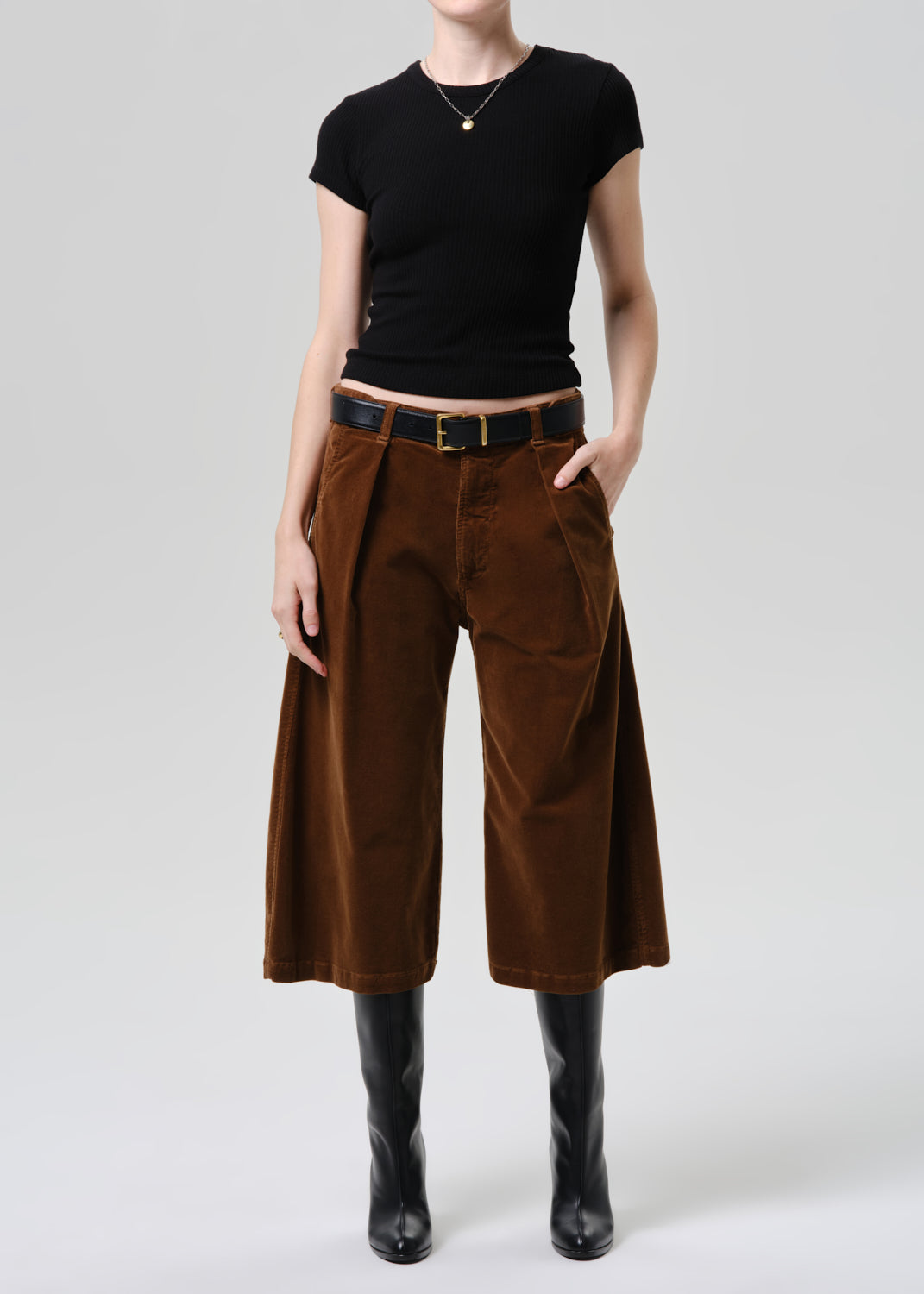 Person wearing a black top and brown wide-leg pants on a grey background.