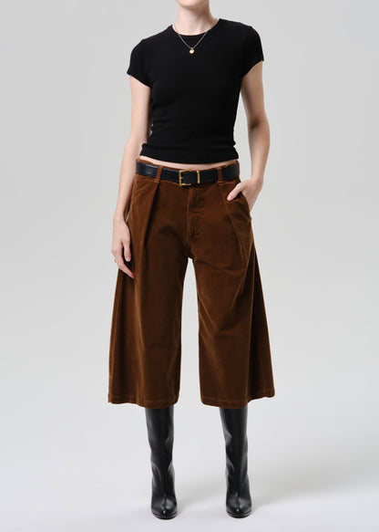 Person wearing a black top and brown wide-leg pants on a grey background.
