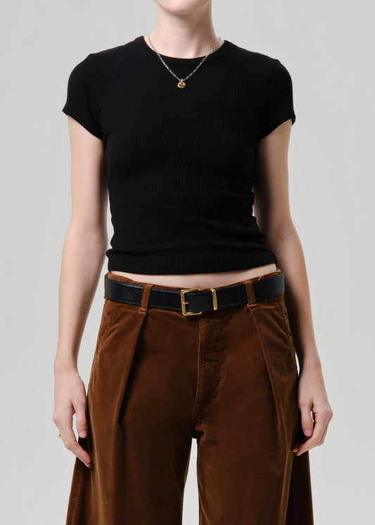A model wearing a black short-sleeve ribbed knit top and brown corduroy trousers with a black belt, shown from the neck down against a grey background.