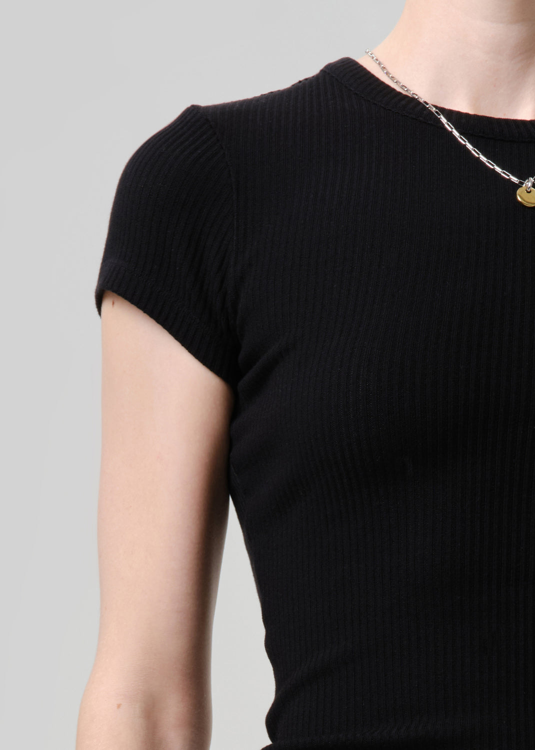Close-up of a person wearing a black short-sleeve ribbed knit top against a grey background.