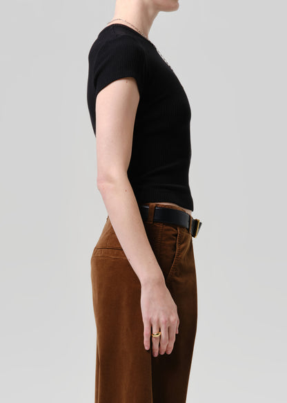 Side profile of a model wearing a black short-sleeve ribbed knit top and brown wide-leg trousers with a black belt, against a grey background.