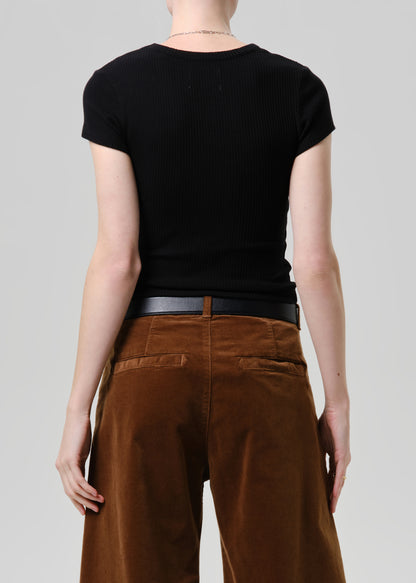 Rear view of a model wearing a black short-sleeve ribbed t-shirt and brown wide-leg trousers with a black belt, against a grey background.