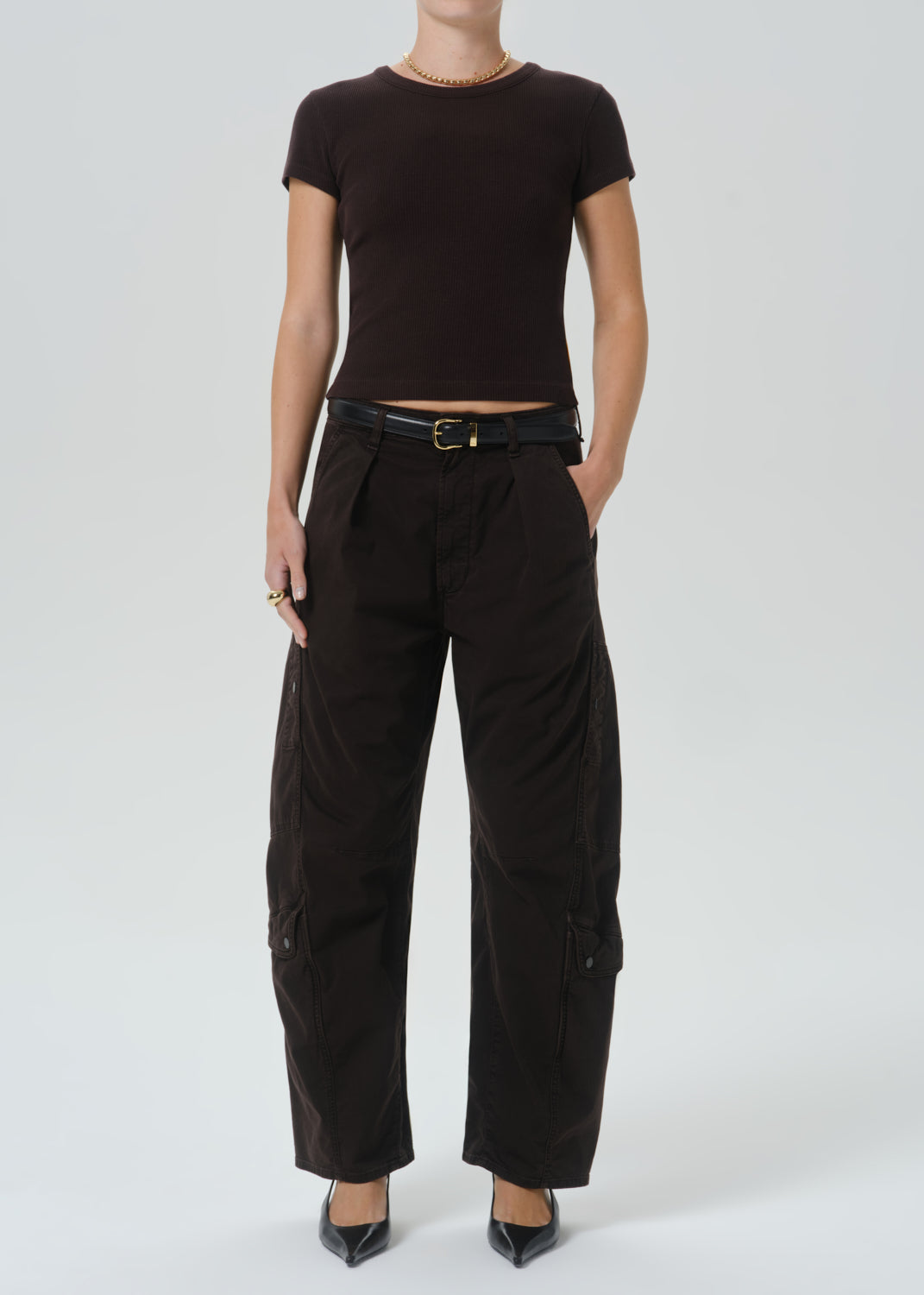 A model wearing a dark brown short-sleeve crop top and black wide-leg cargo pants with a black belt, standing against a grey background.