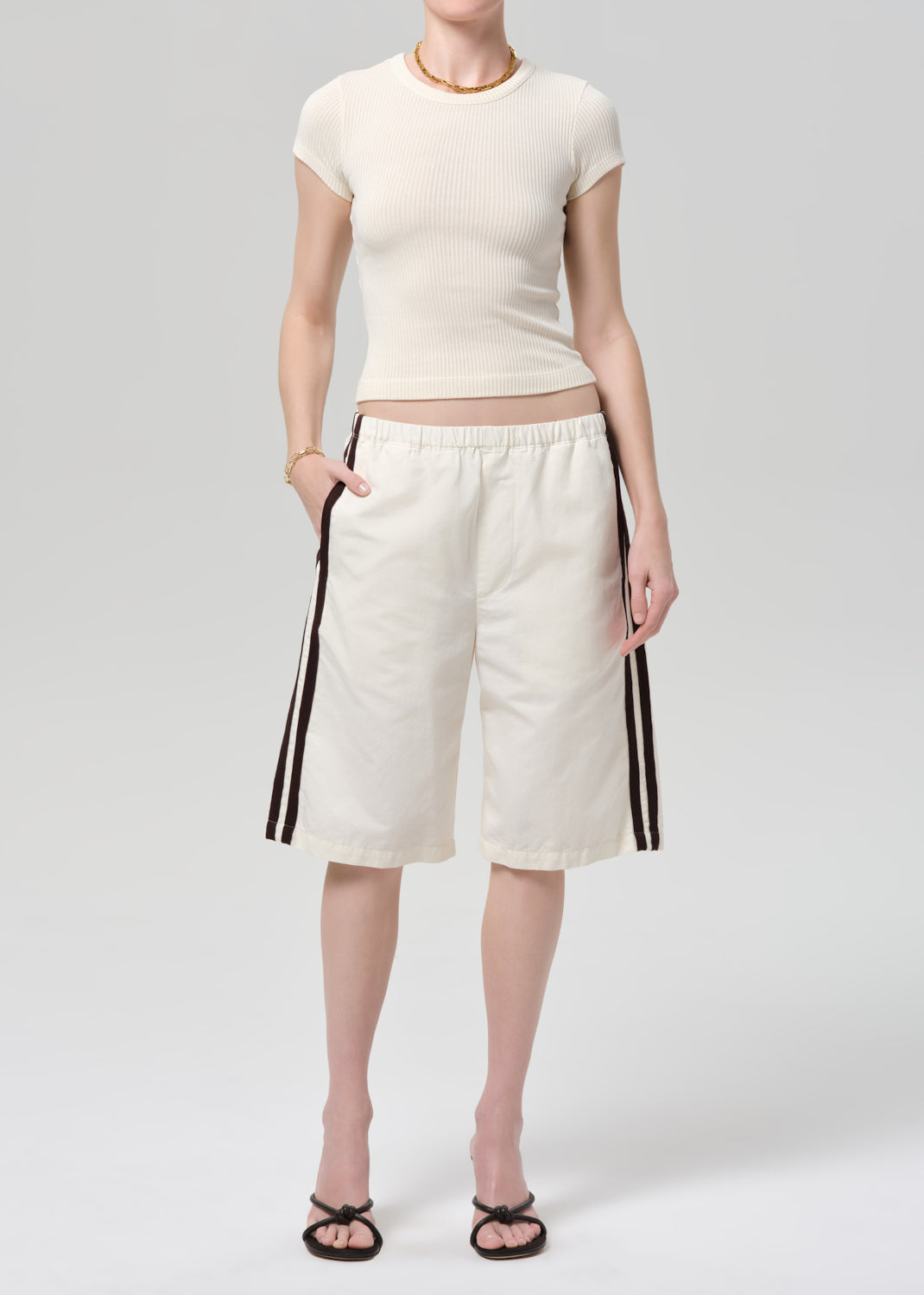 Person wearing a off-white ribbed tee and track shorts on a gray background