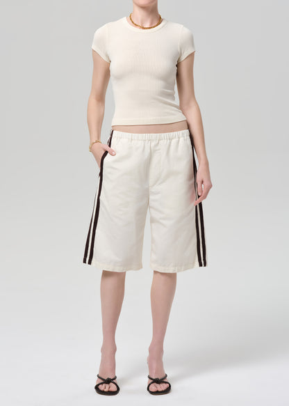 Person wearing a off-white ribbed tee and track shorts on a gray background