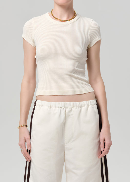 Person wearing a off-white ribbed tee and track shorts on a gray background