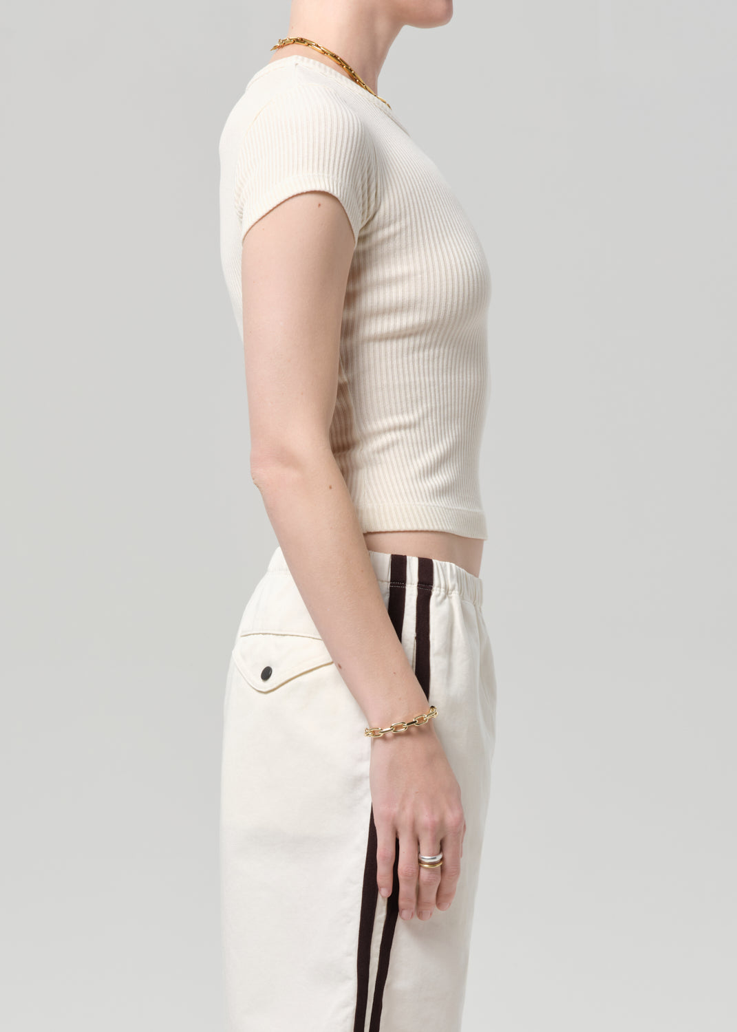 Person wearing a off-white ribbed tee and track shorts on a gray background