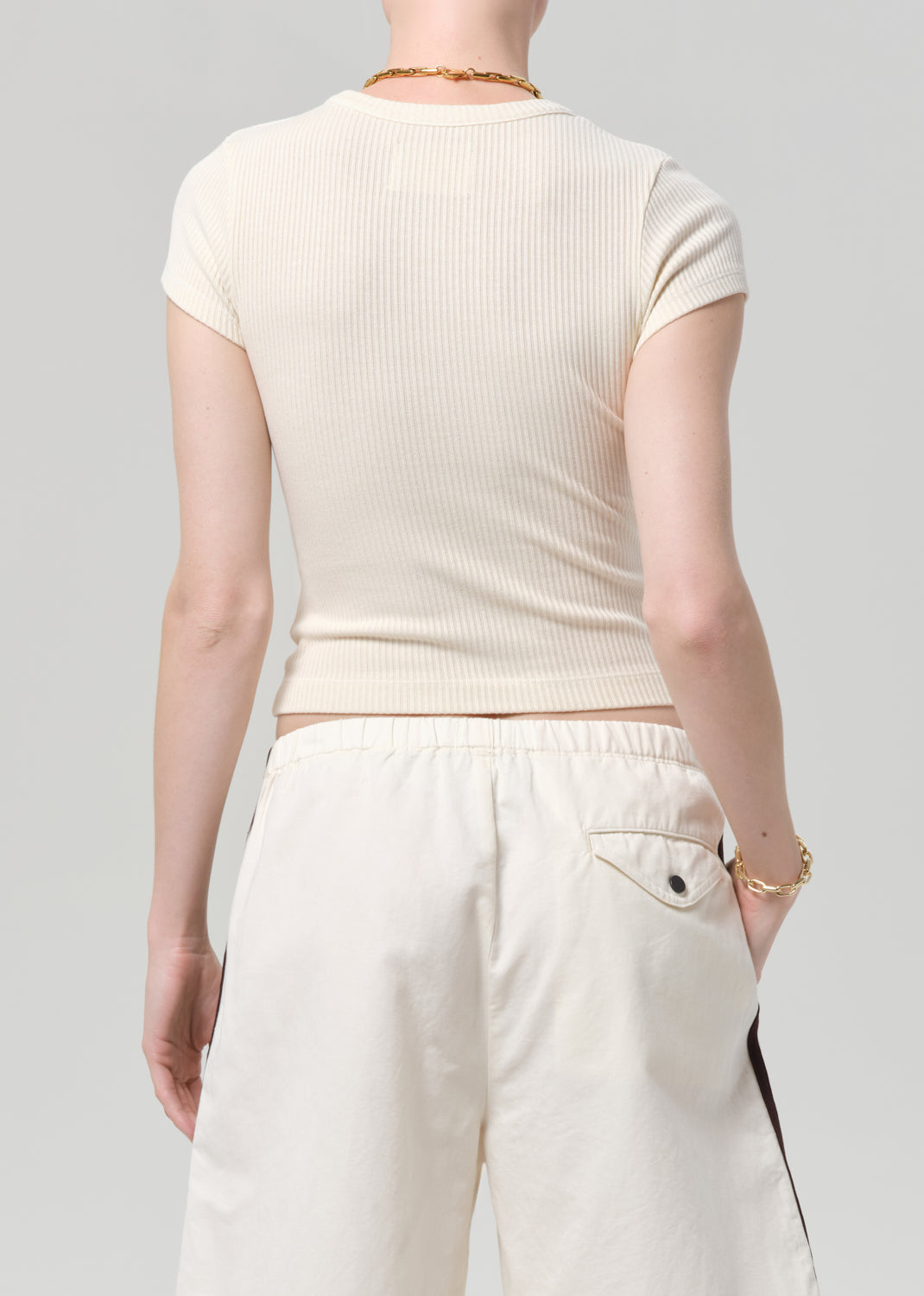Person wearing a off-white ribbed tee and track shorts on a gray background