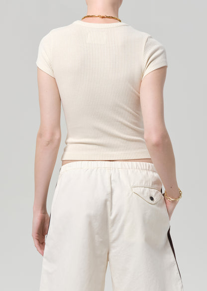 Person wearing a off-white ribbed tee and track shorts on a gray background