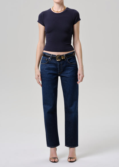 A model wearing dark blue straight-leg jeans with a gold-tone belt, paired with a navy blue short-sleeve top and black sandals, photographed against a grey background.